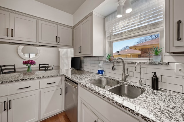 kitchen with a sink, light stone countertops, backsplash, and stainless steel dishwasher