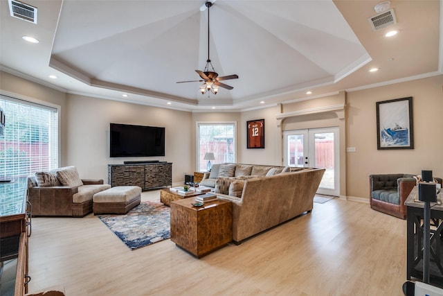 living area with a wealth of natural light, a tray ceiling, visible vents, and light wood finished floors