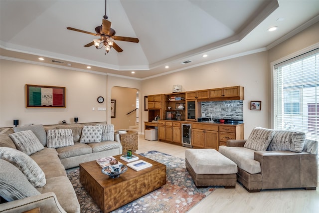 living area with a tray ceiling, wine cooler, arched walkways, and ornamental molding