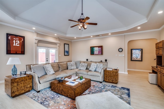 living room featuring arched walkways, light wood finished floors, and a raised ceiling