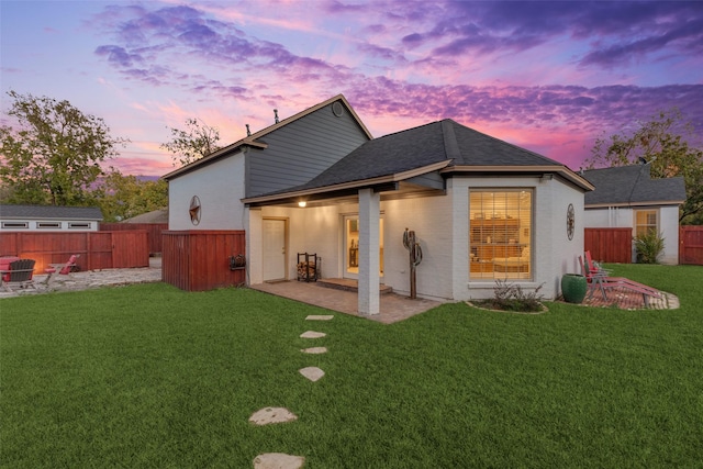 back of property featuring a lawn, fence, roof with shingles, brick siding, and a patio area