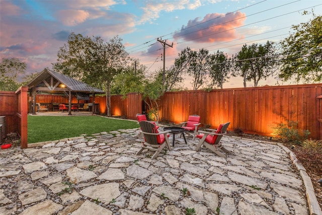 patio terrace at dusk featuring a gazebo, a fenced backyard, an outdoor fire pit, and a yard