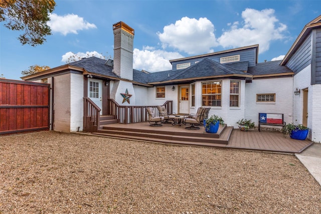 back of property with a deck, fence, brick siding, and a chimney