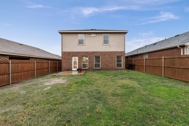 rear view of property with brick siding, a fenced backyard, a lawn, and a patio area