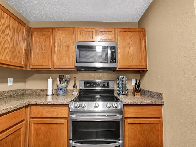 kitchen featuring a textured ceiling, brown cabinetry, a textured wall, and stainless steel appliances