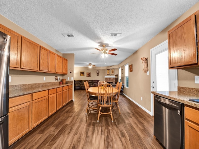 kitchen featuring brown cabinets, a ceiling fan, a textured ceiling, dark wood finished floors, and appliances with stainless steel finishes