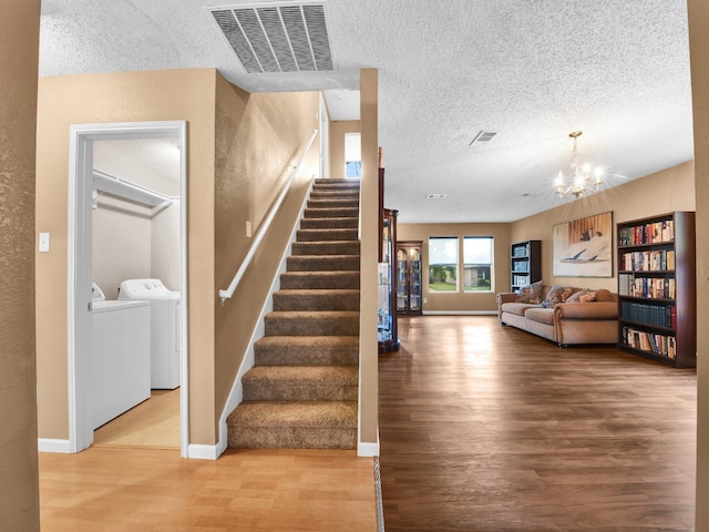 stairs with wood finished floors, visible vents, washing machine and clothes dryer, a textured ceiling, and a chandelier