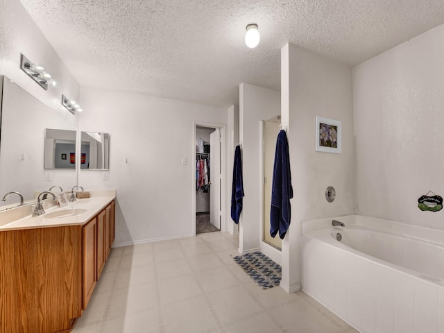 bathroom with a walk in closet, a garden tub, double vanity, a textured ceiling, and a sink