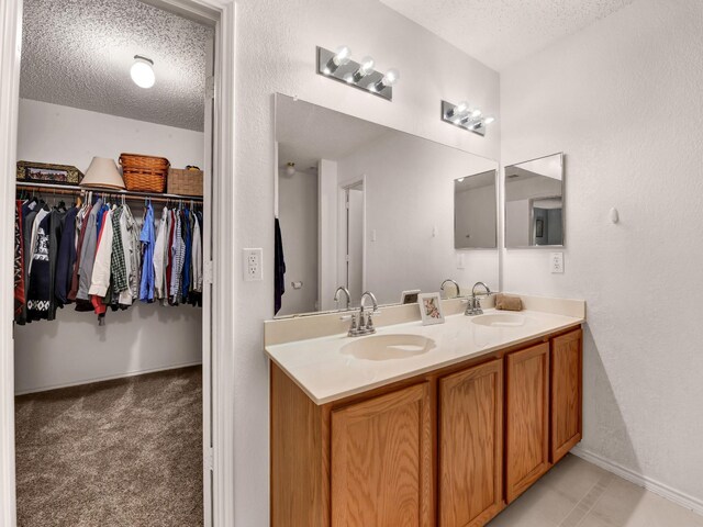 full bath with a textured ceiling, double vanity, a spacious closet, and a sink