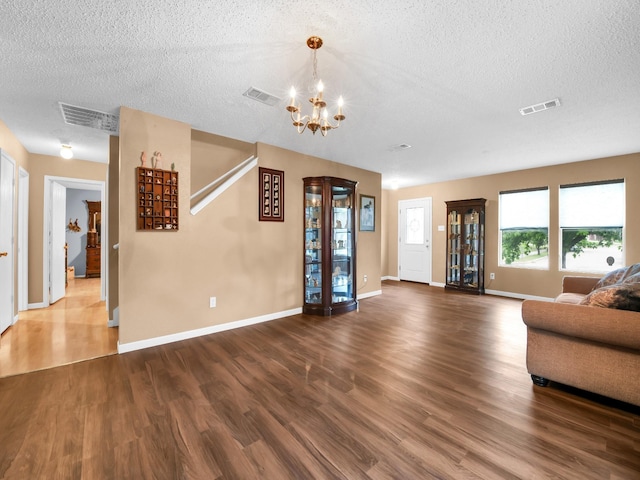 unfurnished living room with a notable chandelier, wood finished floors, and visible vents