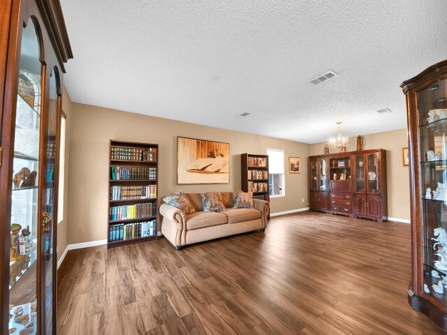 living room featuring visible vents, baseboards, an inviting chandelier, wood finished floors, and a textured ceiling