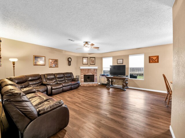 living area featuring baseboards, a brick fireplace, dark wood finished floors, and a ceiling fan