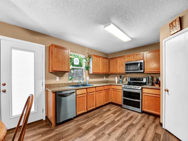 kitchen with light wood-style flooring, a sink, a textured ceiling, appliances with stainless steel finishes, and light countertops