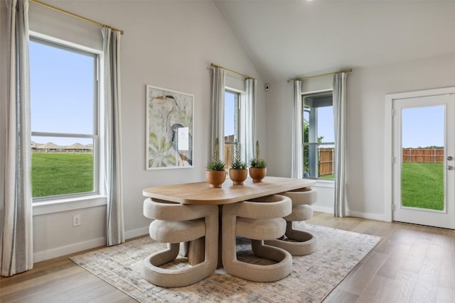 dining space with light wood-type flooring, baseboards, and vaulted ceiling