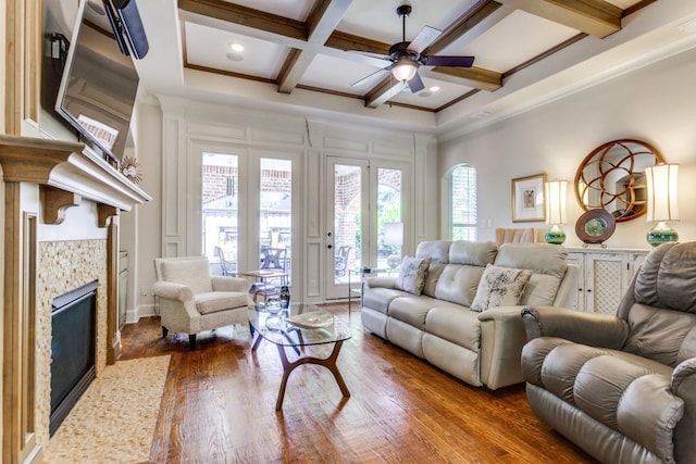 living room with beamed ceiling, coffered ceiling, wood finished floors, a fireplace, and crown molding