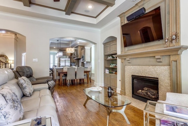 living room featuring wood finished floors, coffered ceiling, beam ceiling, ornamental molding, and a tiled fireplace