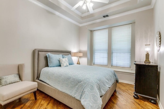 bedroom featuring a tray ceiling, visible vents, wood finished floors, and ornamental molding