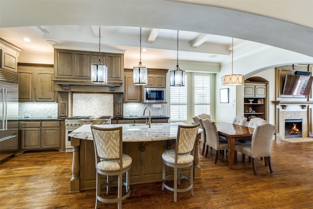 kitchen with beam ceiling, a sink, tasteful backsplash, dark wood finished floors, and built in appliances