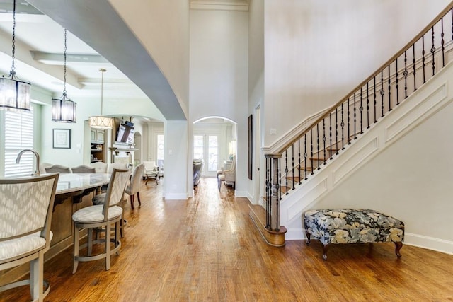 foyer with wood finished floors, arched walkways, a high ceiling, baseboards, and stairs