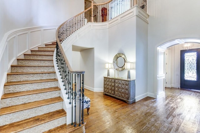 foyer entrance with baseboards, a towering ceiling, wood finished floors, arched walkways, and a decorative wall