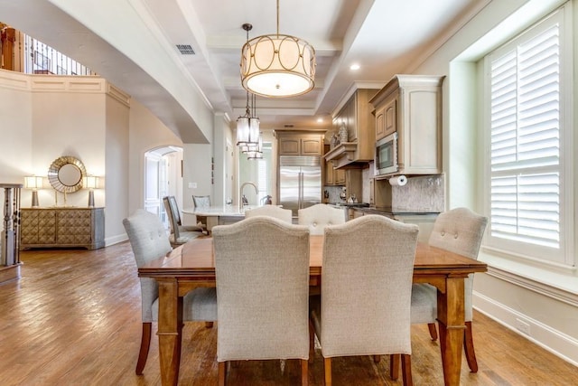 dining area with arched walkways, light wood-style floors, visible vents, and baseboards