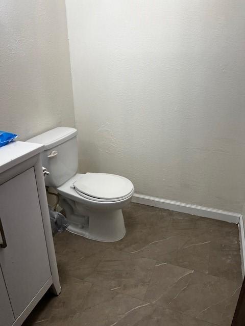 half bath with baseboards, toilet, and vanity