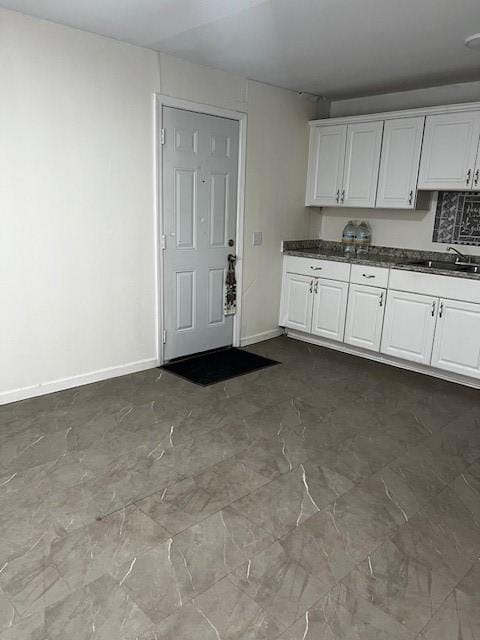 kitchen with dark countertops, white cabinetry, baseboards, and a sink