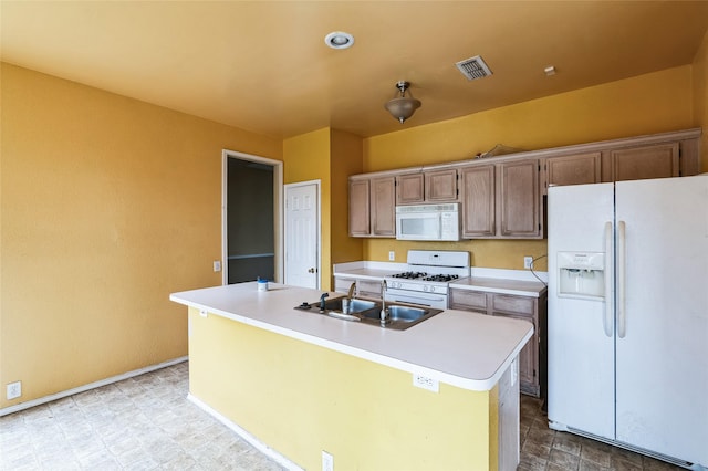 kitchen featuring visible vents, a kitchen island with sink, a sink, white appliances, and light countertops