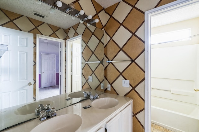 full bathroom with visible vents, double vanity, a sink, a textured ceiling, and a washtub