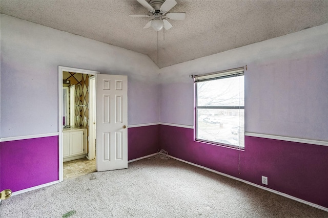 unfurnished room featuring carpet, baseboards, ceiling fan, vaulted ceiling, and a textured ceiling