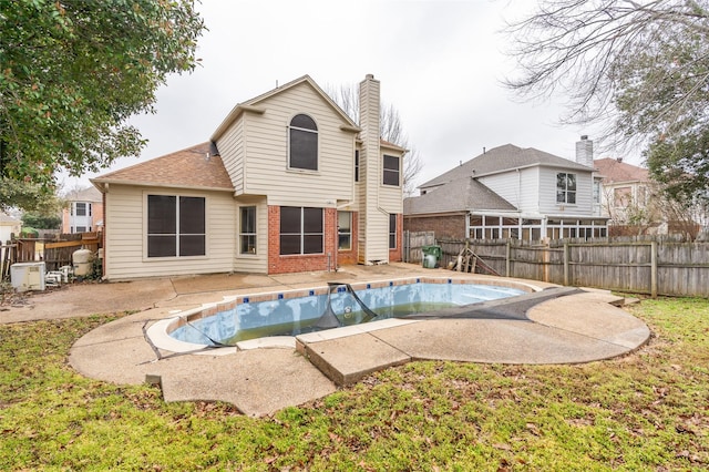 rear view of property with a patio, a fenced backyard, a fenced in pool, brick siding, and a chimney