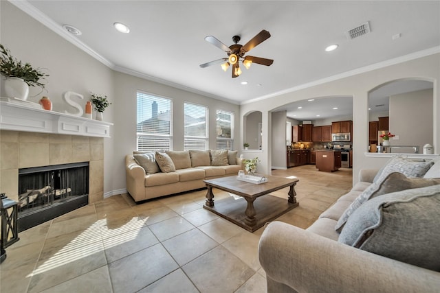 living area featuring a tiled fireplace, ornamental molding, light tile patterned floors, recessed lighting, and a ceiling fan