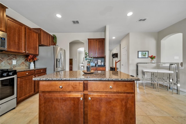 kitchen featuring visible vents, dark stone countertops, backsplash, a center island, and stainless steel appliances