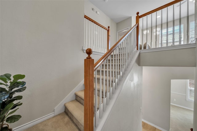 stairway featuring baseboards, a high ceiling, and carpet flooring