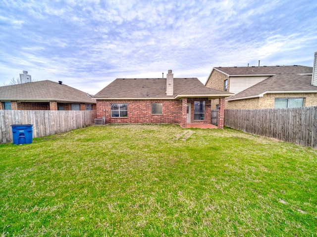 back of property featuring a lawn, a fenced backyard, brick siding, central AC unit, and a chimney