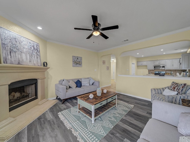 living area featuring arched walkways, a fireplace with raised hearth, wood finished floors, and ornamental molding