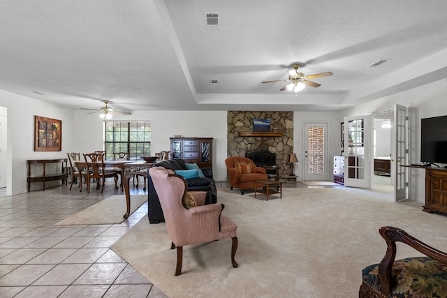 living room with visible vents, a tray ceiling, a textured ceiling, a fireplace, and light tile patterned floors