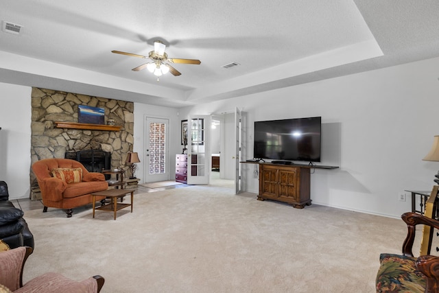 carpeted living area featuring visible vents, a raised ceiling, a textured ceiling, and a stone fireplace