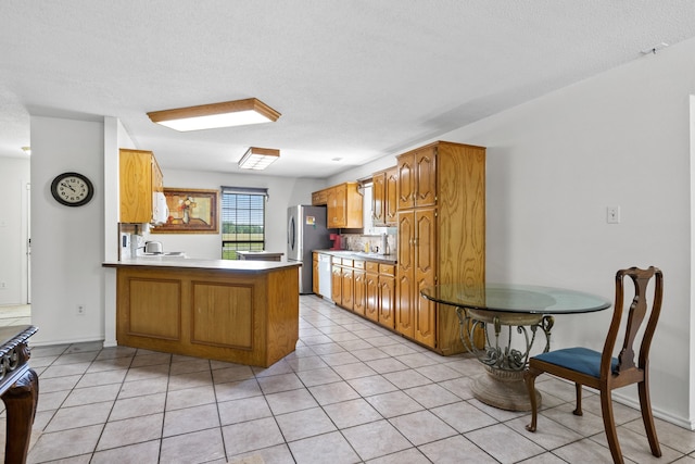 kitchen featuring a peninsula, light tile patterned flooring, freestanding refrigerator, dishwasher, and backsplash