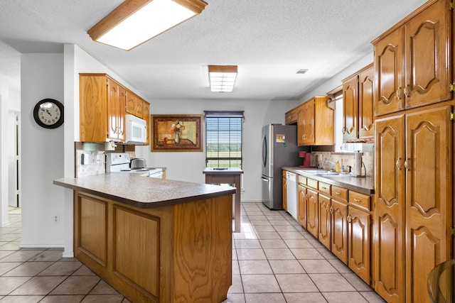 kitchen with white appliances, brown cabinetry, light tile patterned floors, and a peninsula