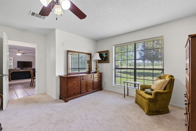 living area featuring visible vents, light colored carpet, light tile patterned floors, a textured ceiling, and a ceiling fan