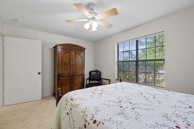 bedroom with light colored carpet, ceiling fan, and a textured ceiling