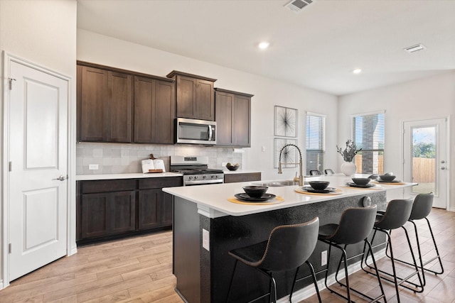 kitchen featuring a breakfast bar area, a kitchen island with sink, a sink, stainless steel appliances, and backsplash