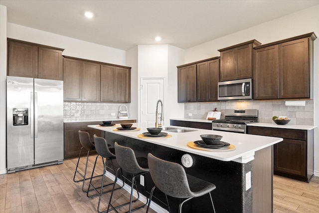 kitchen with a sink, dark brown cabinetry, light wood-style flooring, stainless steel appliances, and a kitchen island with sink