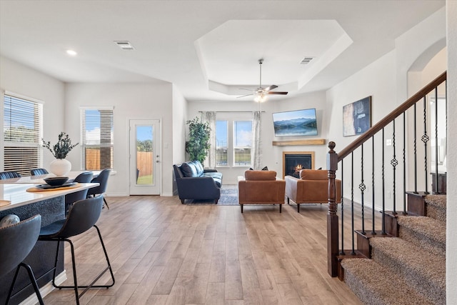 living room featuring a raised ceiling, a warm lit fireplace, visible vents, and light wood finished floors