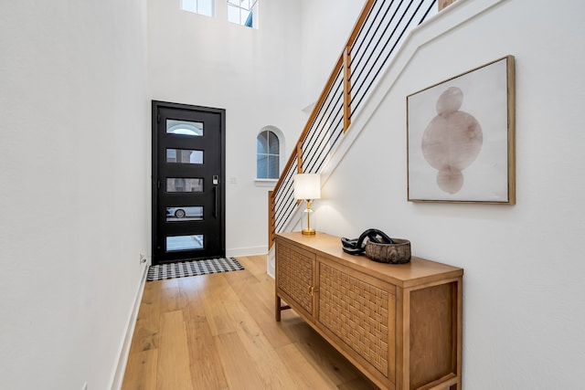 entrance foyer with baseboards, a towering ceiling, stairs, and light wood finished floors