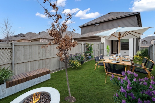 exterior space with a yard, a fenced backyard, roof with shingles, and an outdoor fire pit