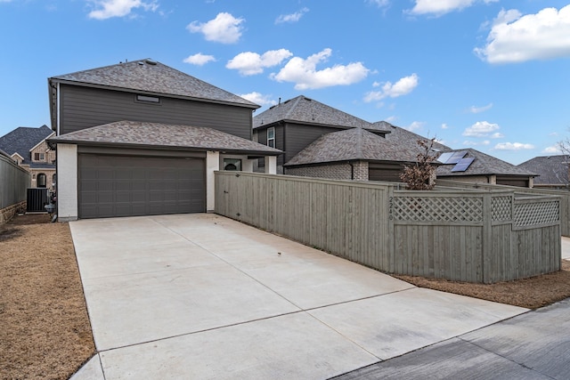 exterior space featuring fence, a shingled roof, concrete driveway, a garage, and central air condition unit