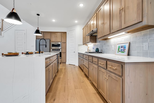 kitchen featuring under cabinet range hood, light countertops, decorative backsplash, light wood-style flooring, and appliances with stainless steel finishes