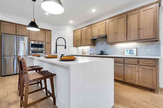 kitchen with under cabinet range hood, stainless steel appliances, light wood-style floors, and decorative backsplash